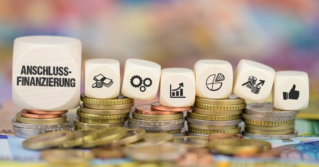 Vergleich der Anschlussfinanzierung: Münzen und Holzblock-Icons symbolisieren Zinsersparnis und Bankenvergleich für Hausbesitzer – Flusche Finance