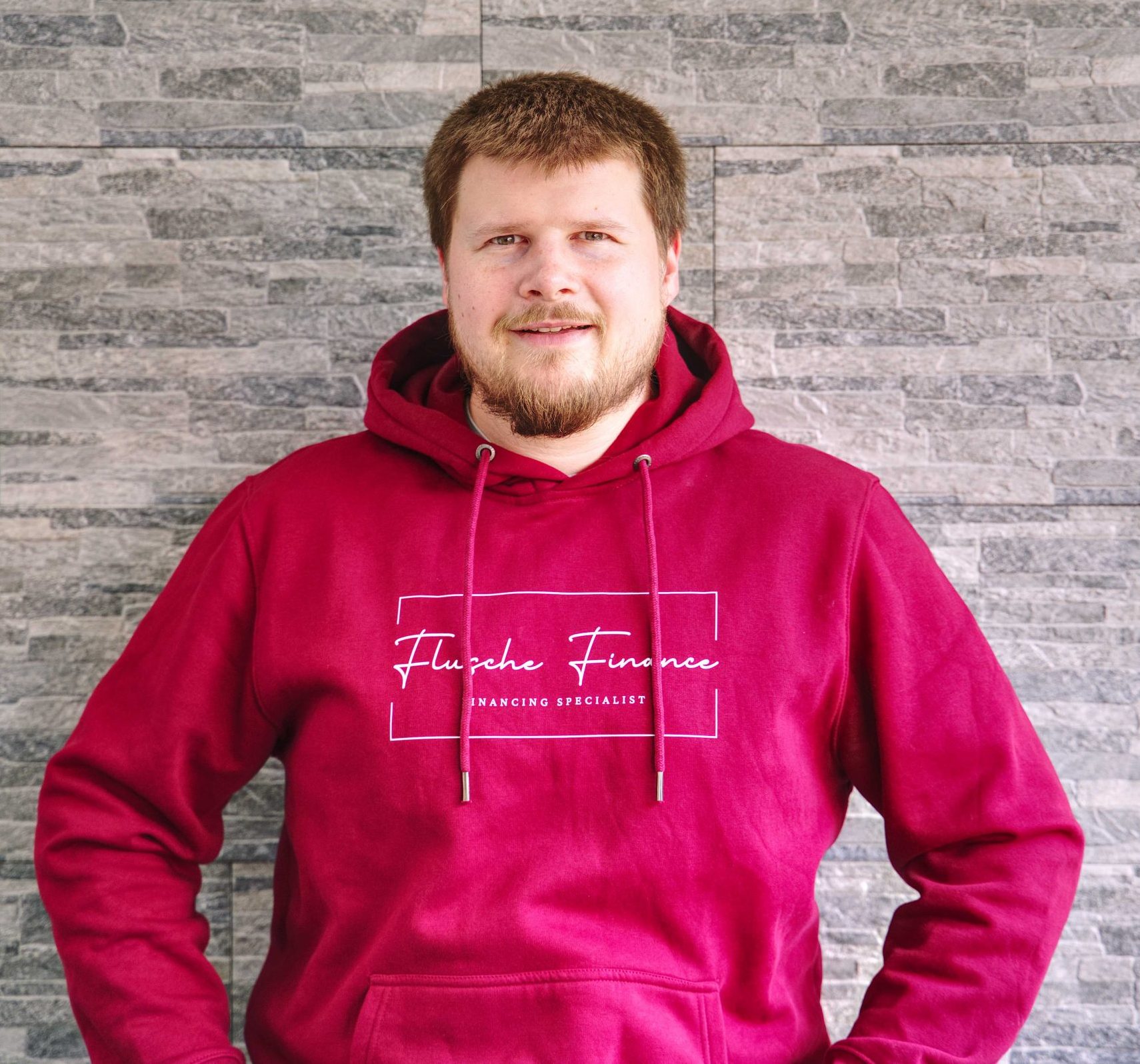 Bild mit Inhaber. Lächelnde Person mit roten Sweatshirt vor grauem Hintergrund.